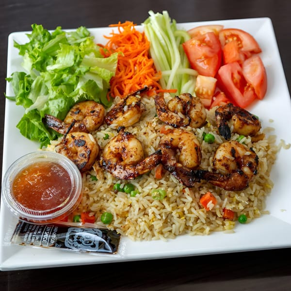 Grilled shrimp with fried rice, fresh lettuce, shredded carrots, cucumber, and sliced tomatoes.