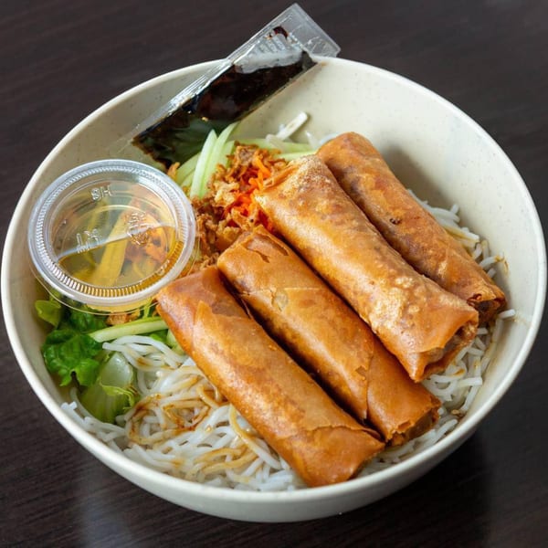 Vietnamese vermicelli bowl with four golden spring rolls, fresh greens, and sauces in a white bowl.