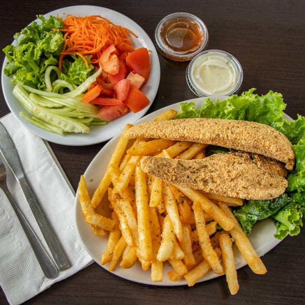 Fried fish fillets with french fries and a side salad with dressing cups on a dark table.