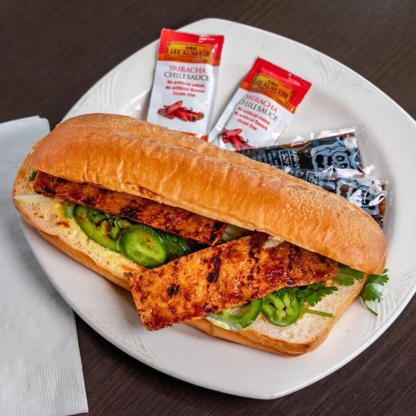 Vietnamese banh mi sandwich with grilled meat, jalapenos, and cilantro, served with sriracha packets.