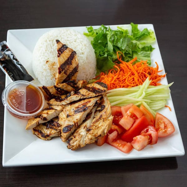 Grilled chicken with rice, lettuce, shredded carrots, cucumber, and diced tomatoes on a white plate.